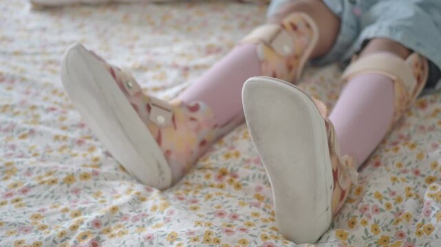 Close up shot of young girl wearing leg braces and pink stockings lying on bed, dynamic video footage capturing her recovery journey