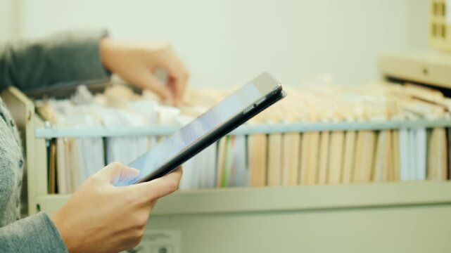 Businesswoman checking documents with tablet in office archive cabinet.