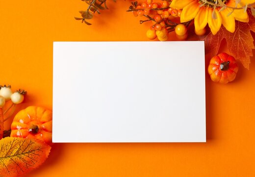 Festive autumn arrangement featuring pumpkins, leaves, berries and white paper card against an orange background. Design for Thanksgiving greeting cards