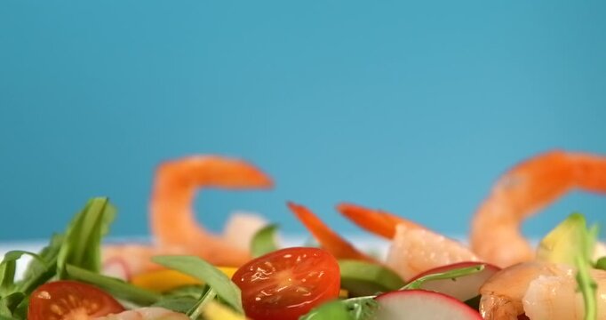 Shrimp falling onto fresh vegetable salad with avocado in slow motion