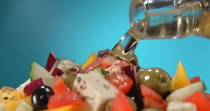 Olive oil pouring onto fresh greek salad with feta cheese olives tomato and cucumber in slow motion