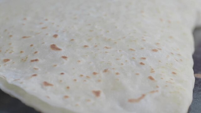 Fresh dough baking on flat grill surface as professional chef flips thin handmade tortilla.