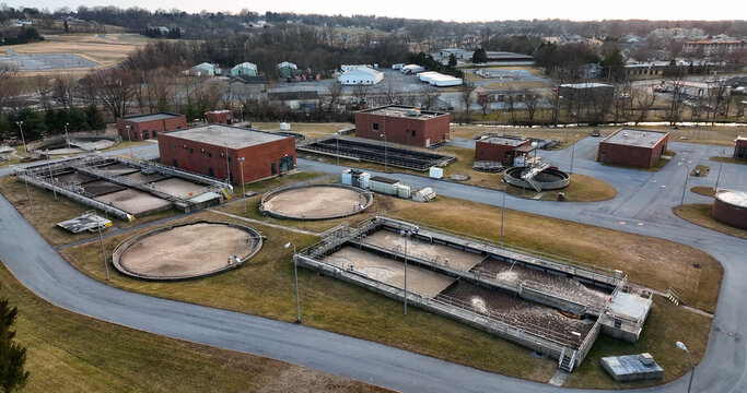 Aerial view of a wastewater treatment plant with circular sedimentation tanks, rectangular aeration basins, and brick buildings in a suburban setting in Lititz, Pennsylvania, United States.