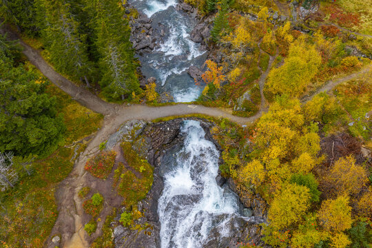 Aerial view of an old stone bridge crossing a rushing waterfall surrounded by vibrant autumn foliage and evergreen trees in Fjord, More og Romsdal, Norway.