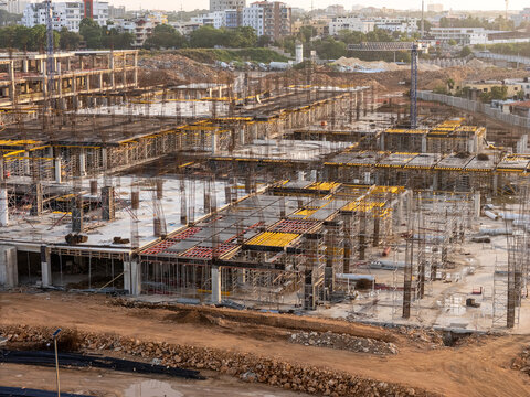 Aerial view of a large construction site with concrete foundations, steel rebar structures, and yellow formwork under a clear sky in Santo Domingo Este, Santo Domingo Provinc, Dominican Republic.