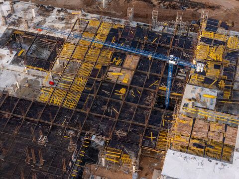 Aerial view of a large construction site featuring yellow formwork, steel reinforcement grids, and a blue tower crane in Santo Domingo Este, Santo Domingo Province, Dominican Republic.