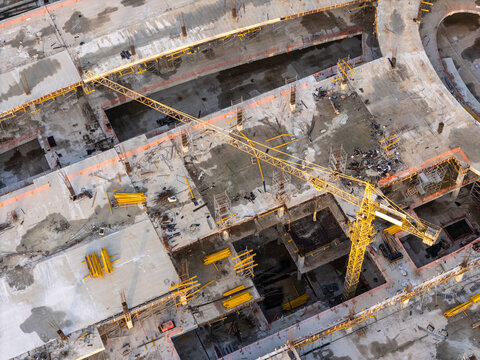 Aerial view of a construction site with a yellow tower crane, concrete foundations, steel reinforcements, and building materials in Santo Domingo Este, Santo Domingo Province, Dominican Republic.