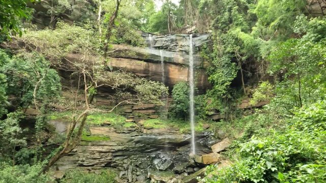 Tranquil waterfall flowing over rocky cliffs amidst dense green jungle vegetation in Thailand