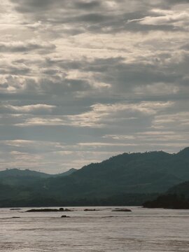 Serene landscape of the Mekong River, green mountains, and cloudy sky in rural Thailand.