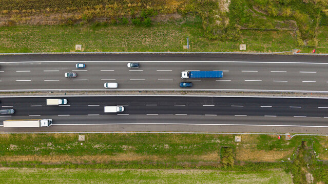 Aerial View of Highway Traffic: An aerial perspective captures the flow of vehicles on a multi-lane highway, with trucks and cars navigating the road amidst green rural landscapes.