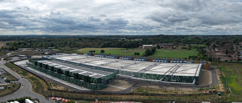 Aerial view of a large modern data center facility with green and grey industrial architecture, surrounded by roads and green fields in the United Kingdom.