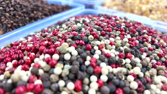 Assorted peppercorns and spices displayed in plastic containers at local traditional market.
