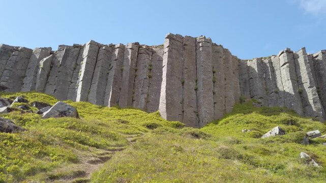 Gerduberg basalt cliff on the Snaefellsnes peninsula, Iceland, a long wall of tall hexagonal dolerite columns rising above a green grassy slope under a blue sky.