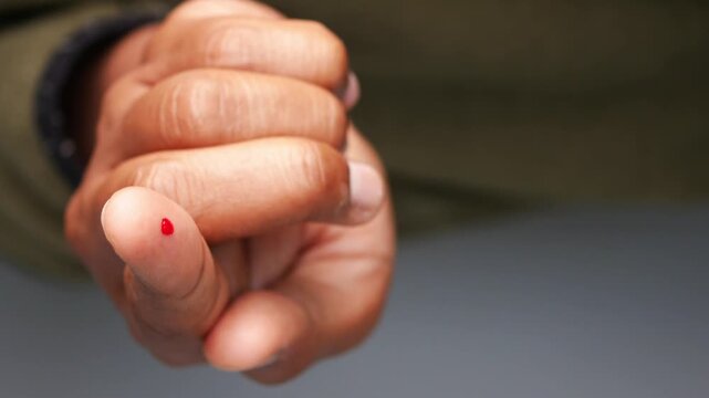 Drop of blood on finger tip close up for diabetes monitoring or health checkup diagnostics.