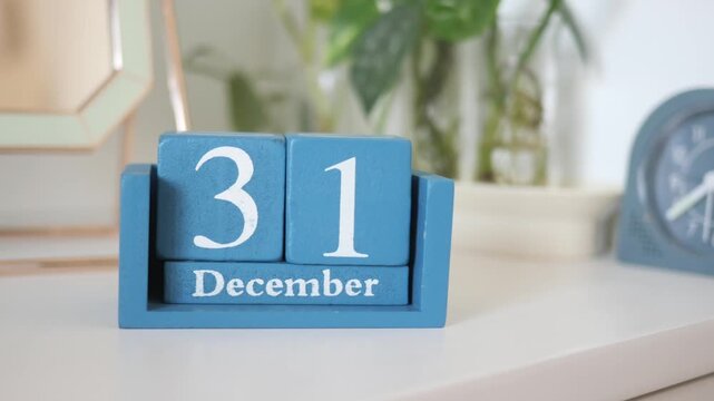Blue wooden calendar shows december 31st with vintage alarm clock in soft focus.