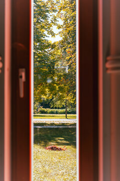 A vertical glimpse of a bright landscaped park with golden trees and fallen leaves appears between dark reddish wooden door frames.