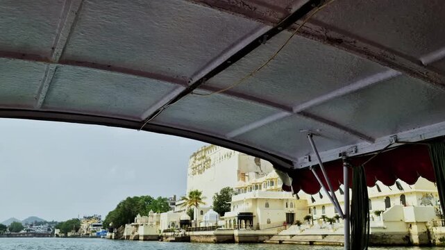 A boat canopy frames the pale waterfront walls and terraces of the City Palace complex on Lake Pichola in Udaipur.