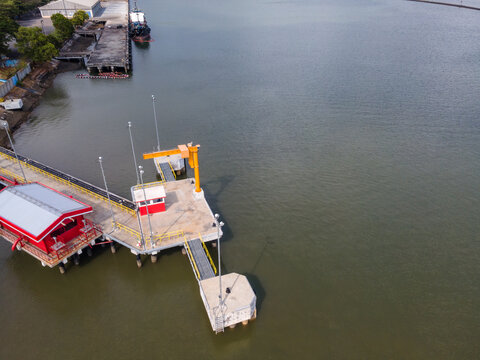 Aerial view of Sleko Harbor featuring a yellow crane and red industrial buildings on a concrete pier extending into the calm water in Cilacap, Central Java, Indonesia.