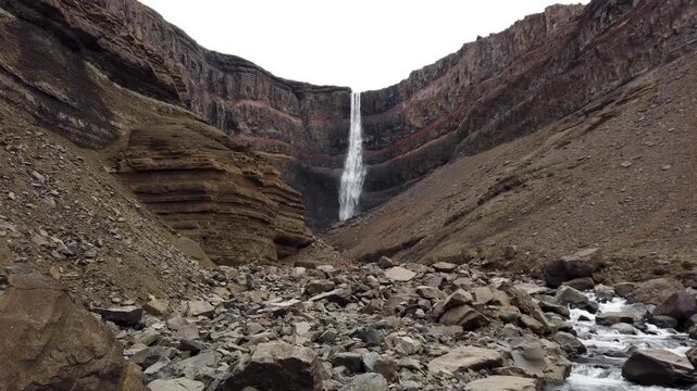 Hengifoss waterfall in Fljotsdalur, Iceland, one of the tallest in the country, dropping between basalt cliffs striped with red clay layers above a rocky stream.