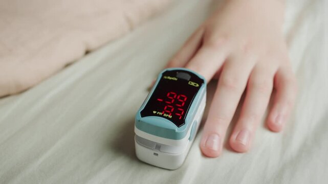 Digital pulse oximeter monitoring oxygen saturation level on human finger during resting.