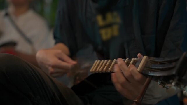close view musician hands playing traditional thai phin stringed instrument, artist fingers strumming frets on acoustic folk song performance 4k