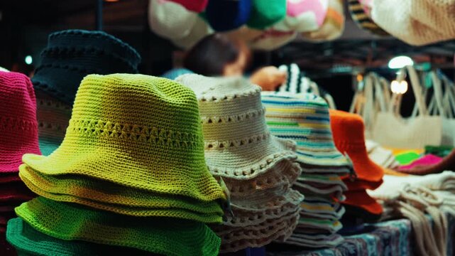 knitted bucket hats stacked at night market stall, colorful handmade crochet headwear souvenirs for sale in street bazaar 4k