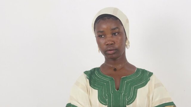 Young African woman in a green and white embroidered traditional outfit, studio portrait.
