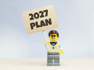 Obraz premium Indonesia - June 12, 2026 : Mini toy of action figure at table with blurred background. Business Miniature photography concept design. Minifigure of people with 2027 PLAN text at paper poster banner.