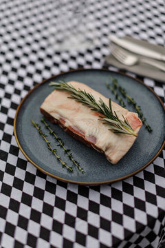 Raw lamb meat on a dark ceramic plate, garnished with fresh rosemary and thyme over a black-and-white checkered tablecloth