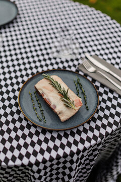 Raw lamb meat on a dark ceramic plate, garnished with fresh rosemary and thyme over a black-and-white checkered tablecloth