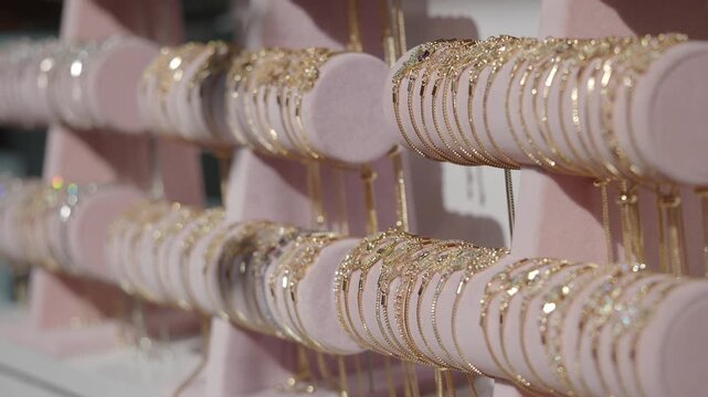 Gold bracelet display with sparkling jewels on pink velvet rollers in jewelry shop window.