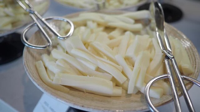 Close up video of sliced cheese sticks served on a plate with tongs.