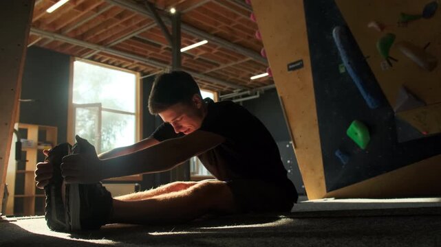 Sportsman sits on floor performing stretching exercise in fitness center. Man touches feet improving overall body flexibility
