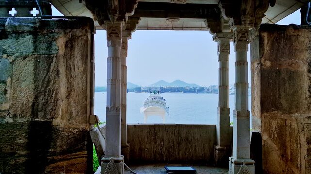 Carved columns frame a view of Lake Pichola and a small white pavilion from inside Jag Mandir in Udaipur.