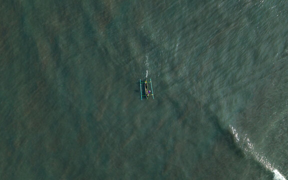 Aerial view of a traditional outrigger boat with fishermen returning from the sea across the deep blue ocean waters in Kecamatan Jembrana, Bali, Indonesia.