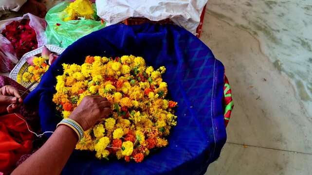 Hands gather yellow and orange marigolds from a blue cloth-lined basket while preparing flower garlands in Udaipur.