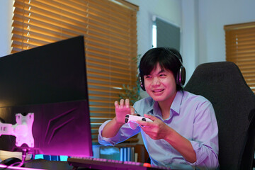 Excited young Asian gamer smiles while holding a controller at a neon lit PC gaming desk, ideal for gaming lifestyle and entertainment concepts © Stella 16