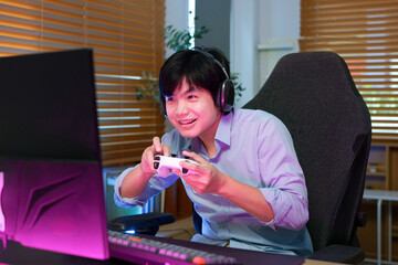 Excited young Asian gamer smiles while holding a controller at a neon lit PC gaming desk, ideal for gaming lifestyle and entertainment concepts © Stella 16