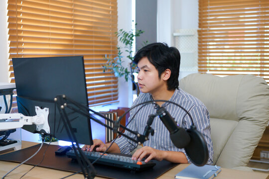Young Asian blogger man checking script on computer before recording podcast for his social media with a condenser microphone, ideal for remote work, podcasting, or streaming concepts