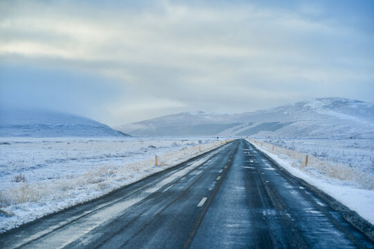 Scenic icy winter road driving in extreme conditions on the Iceland Ring Road. Snow-covered highway with mountain landscape and overcast sky.