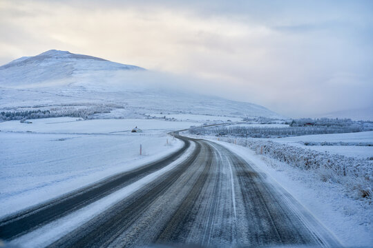 Scenic winding icy road curving through snow-covered landscape towards mountains in Iceland winter. Arctic highway road trip and self-drive travel adventure.