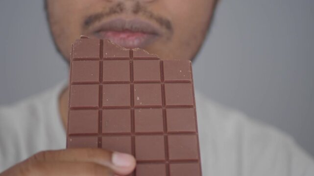 Person eating chocolate bar, close up of mouth and sweet treat.
