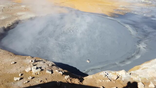 Mud pot bubbling in the Hverir geothermal field below Namafjall ridge near Lake Myvatn, Iceland, grey boiling mud steaming in the sunshine.