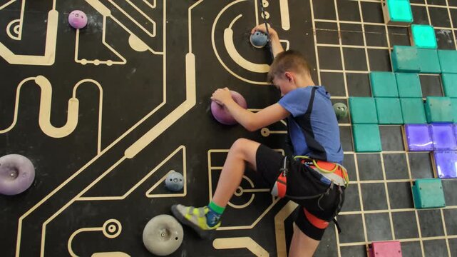 Boy climbs painted wall grabbing round stones. Young athlete in sportswear concentrated working out in gym slow motion
