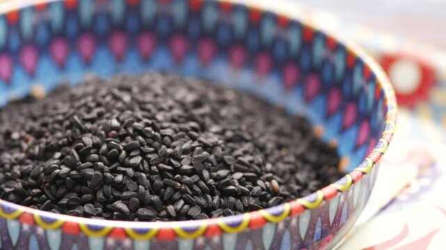 A close up video of nigella seeds in a bowl with a colorful patterned rim.