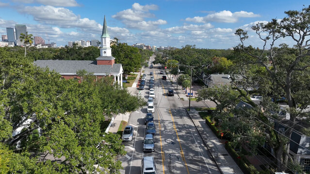 Aerial view of the historic Hyde Park neighborhood featuring a church, tree-lined streets, traffic, and the Tampa skyline in the distance under a blue sky in Tampa, Florida, United States.