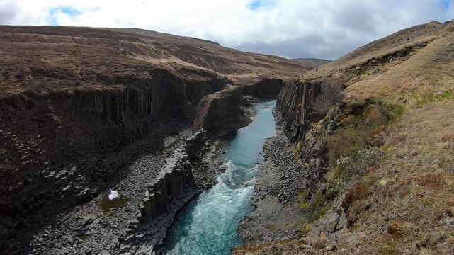Aerial view along Studlagil canyon, Iceland, where a glacial river flows through a deep gorge lined with dark hexagonal basalt columns.