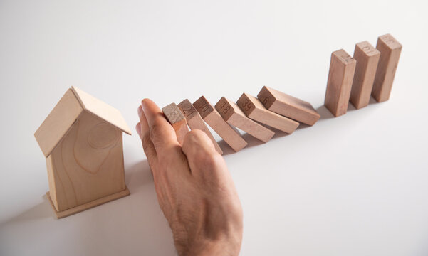 Male hand stopping wooden blocks from falling on house.