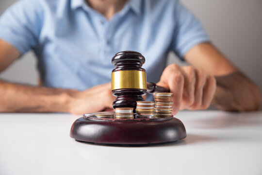 Male hand showing judge gavel over coins.