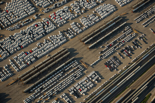 Aerial view of rows of new cars parked in a large distribution facility with freight trains nearby in Kansas City, Missouri, United States.